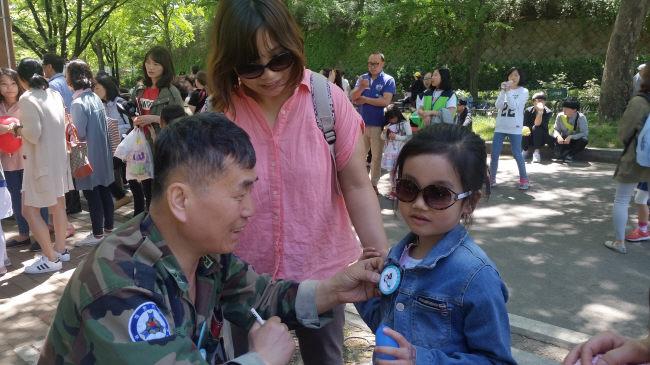 대한민국부사관총연맹 봉사자가 보라매공원에서 어린이의 가슴에 캐릭터 이름표를 달아주고 있다.       
대부총 제공