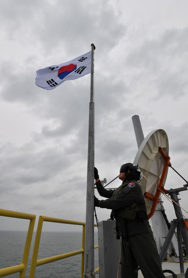 이어도 해양과학기지에 태극기 ‘펄럭’  해군 해상작전헬기 조작사가 독도함과 최영함에 분승한 3군 사관생도들이 지켜보는 가운데 이어도 해양과학기지의 태극기를 교체한 뒤 게양하고 있다.