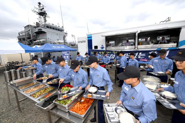15일 경남 창원 진해군항 부두에서 해군 고준봉함 장병들이 배식대에 차려진 음식을 식판에 담고 있다. 해군은 이달부터 함정 승조원 전투력 회복을 위해 대형 취사 트레일러를 활용한 함정 급식지원을 시범 운영한다.  해군 제공 