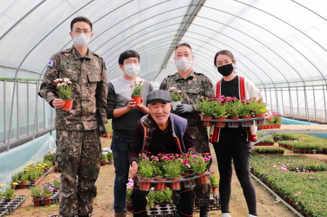 육군5군단 심영보(대위) 환경보전장교와 포천시 농업기술센터 박민철 주무관, 정광수(원사) 동원소요계획부사관, 성주희(군무주무관) 환경담당(뒷줄 왼쪽부터)이 부대 인근에서 화훼농가를 운영하는 백경열(맨 앞) 씨와 함께 화초를 들어보이며 환하게 미소 짓고 있다.  부대 제공