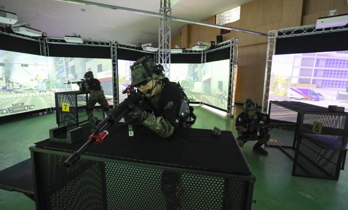부산여단 장병이 가상현실 영상모의 사격장에서 모의총기와 가상현실 장비를 착용한 채 대항군을 조준하고 있다.