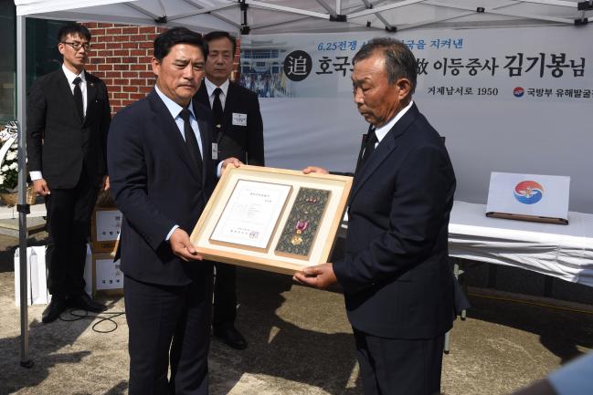 허욱구(왼쪽) 국방부 유해발굴감식단장이 8일 거행된 고 김기봉 이등중사 호국의 영웅 귀환행사에서 김 이등중사의 아들 김종규 옹에게 호국의 얼 함을 전달하고 있다.   국방부 제공