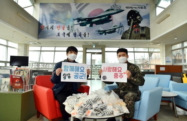 공군19전투비행단 ‘코로나 극복! 3차 충주지역 사랑의 날’을 맞아 한 장병이 간식을 배달하기 위해 부대를 방문한 인근 외부업체 관계자와 함께 응원의 메시지를 들어 보이고 있다.  사진 제공= 지준오 중사 