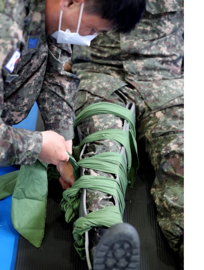 2021년 비행단 기본훈련 종합 경연대회 응급처치 평가에서 한 참가자가 5개의 삼각건을 이용해 상대방의 골절부위에 매듭을 묶고 있다.  