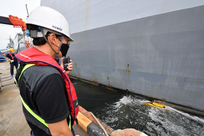 해군군수사령부 정비창 근무자가 수중 선체 청소로봇 작업 상황을 현장 감독하며 운용실에 보고하고 있다.