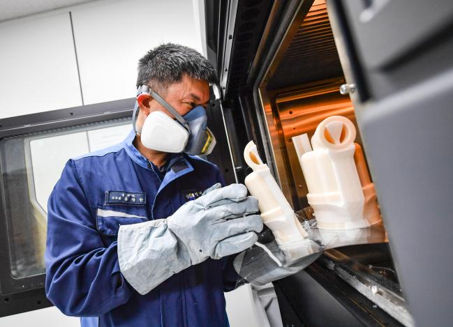 해군군수사 정비창 윤창한 군무주무관이 산업용 방진마스크를 착용하고, 대형 3D 프린터를 활용해 제작한 부품을 살펴보고 있다.