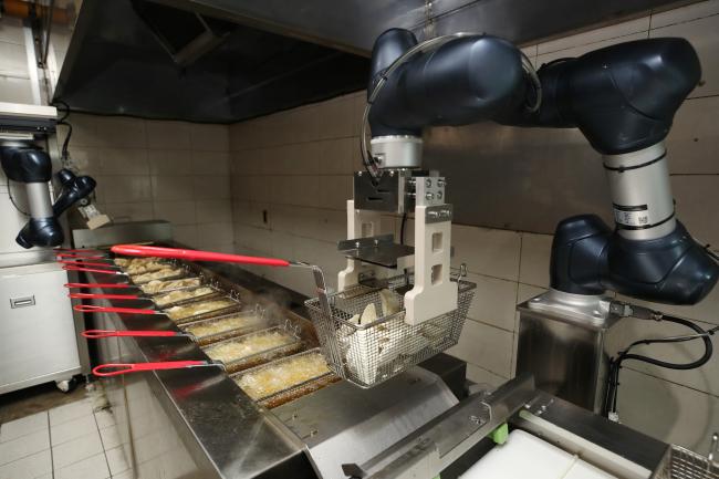 튀김 공정에 투입돼 끓는 기름에 만두를 옮겨 넣을 준비를 하고 있는 다관절 협동로봇(왼쪽)과 뜨겁게 달궈진 400인분 솥에서 된장국을 휘젓고 있는 직교로봇(오른쪽). 튀김에는 4대의 로봇이 투입되는데, 협동로봇이라는 이름처럼 다른 로봇이 컨베이어에 튀김 용기를 내려놓을 때까지 기다리기도 하고, 로봇 팔을 흔들어 기름을 털어내는 모습이 이채롭다.