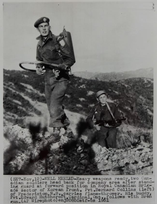 1951년 11월 12일, 중화기로 무장한 캐나다군인들이 한국 전선의 전방에서 경비를 서고 부대로 복귀하고 있다. 화염방사기를 들고 있는 버나드 콜린(왼쪽)과  경기관총을 들고 있는 에드워드 허치크로프트. 