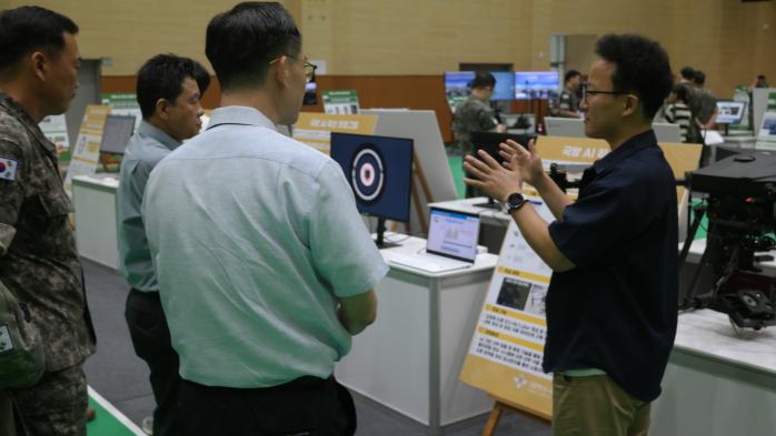 정보통신기획평가원의 한 담당자(맨 오른쪽)가 지작사 AI 성과물 전시장에서 AI 기능을 활용한 드론의 표적 식별 기술에 대해 설명하고 있다. 국방부 제공