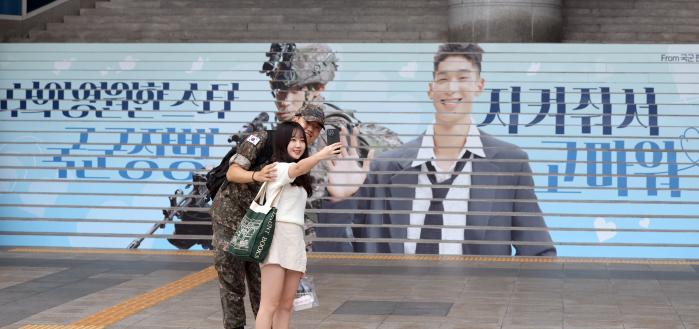 국방부가 국민 참여 오프라인 이벤트 ‘군데군대 군지순례’ 의 하나로 서울 용산역 광장에 게시한 아이디어형 옥외광고 '믿음직한 국군이 국민과 늘 함께' 앞에서 국군 장병이 기념사진을 찍고 있다.