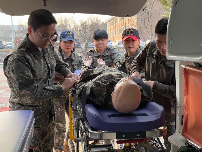 국군의무학교 ‘전투현장 응급처치 참여형 교육 프로그램’에 참여한 건양대 학생들이 의무학교 장병과 함께 환자 모형을 구급차에 싣고 있다. 사진 제공=박현수 대위