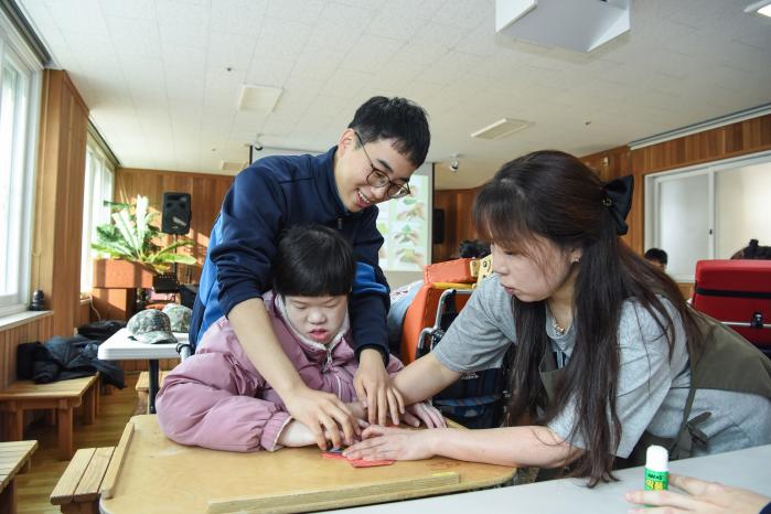 공군1미사일방어여단 장병이 23일 중증장애인 거주 시설에서 복주머니 만들기 활동을 보조하고 있다. 사진 제공=백진현 중사