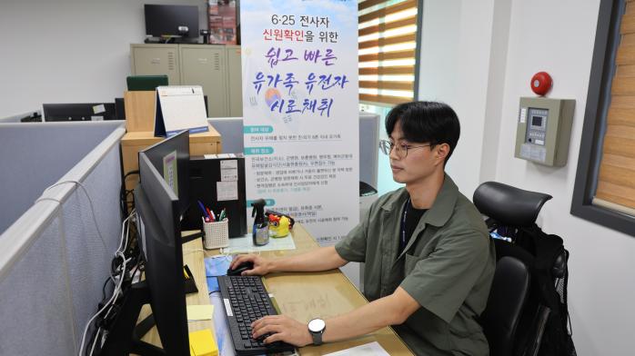 육군5군단 김유빈 군무주무관이 6·25전쟁 전사자 유가족 유전자(DNA) 시료채취 홍보 배너를 배경으로 업무를 하고 있다.