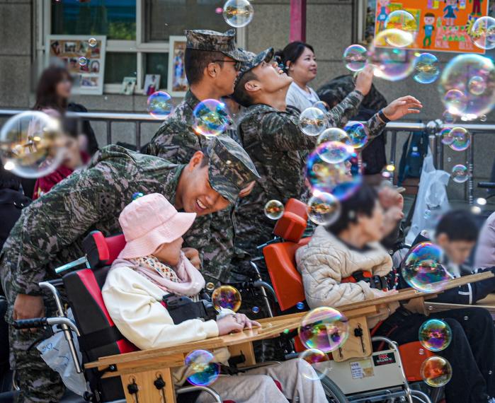 해병대2사단 장병들이 지역 복지시설에서 개최한 축제에 봉사자로 참여해 휠체어 이용자들이 행사를 즐길 수 있도록 돕고 있다. 부대 제공