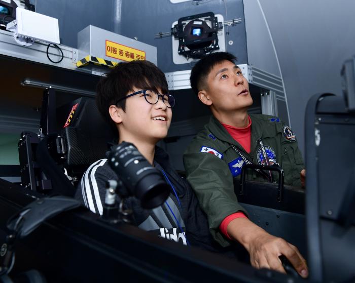 21일 공군3훈련비행단이 한국항공우주소년단을 대상으로 진행한 부대견학에서 참가 단원이 KT-1 항공기 시뮬레이터를 체험하며 조종사의 설명을 듣고 있다. 사진 제공=양하준 하사