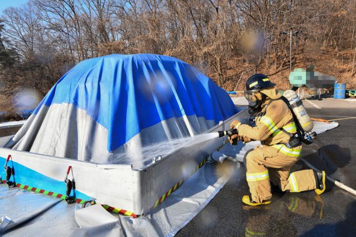 공군8전투비행단이 27일 기지 주차장에서 전기차 화재진압 훈련을 실시한 가운데 장병들이 산소 차단용 덮개로 차량을 덮은 뒤 이동식 소화수조에 물을 채우고 있다. 부대 제공