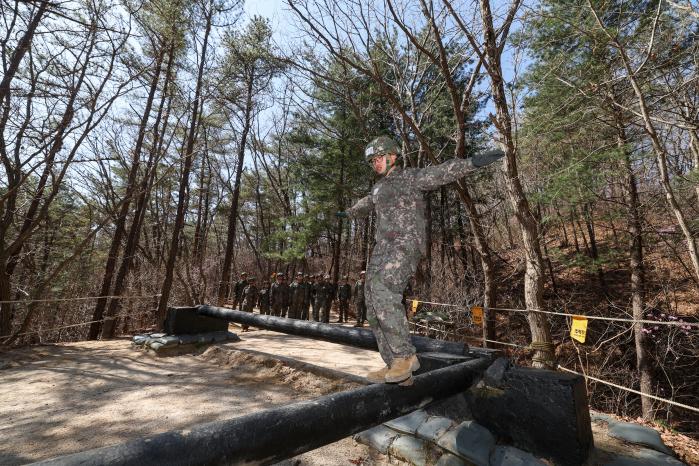 한 장병이 전우들의 응원 속에 외나무다리 장애물을 극복하고 있다.