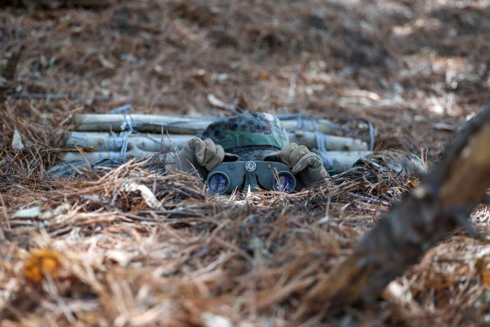 한 장병이 우거진 수풀 사이 숨겨진 은거지 안에 들어가 정찰감시를 하고 있다.