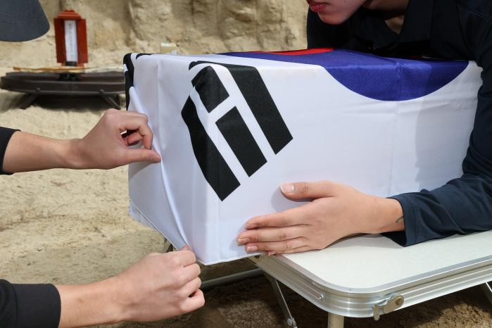 유해를 담은 관에 태극기를 감싸는 모습.