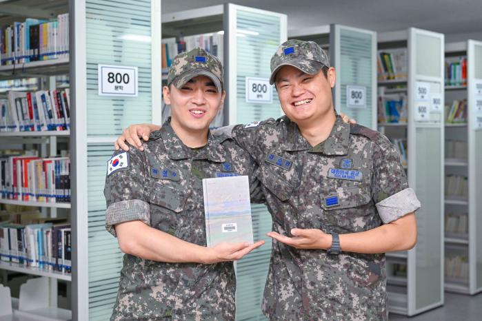 공군19전투비행단 ‘독서는 전우애를 싣고’ 행사에 참여한 감수빈(오른쪽) 상병이 동기생 하상수 상병과 함께 책을 들고 웃고 있다. 사진 제공=윤요한 중사