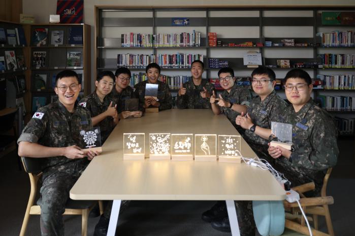 공군5공중기동비행단 장병들이 ‘한 총, 한 책’ 프로젝트의 하나로 참여해 만든 독서 무드등을 선보이며 환하게 웃고 있다.